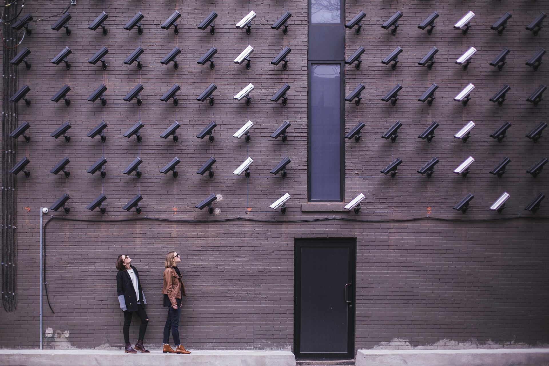 People looking up at tons of cameras on a building