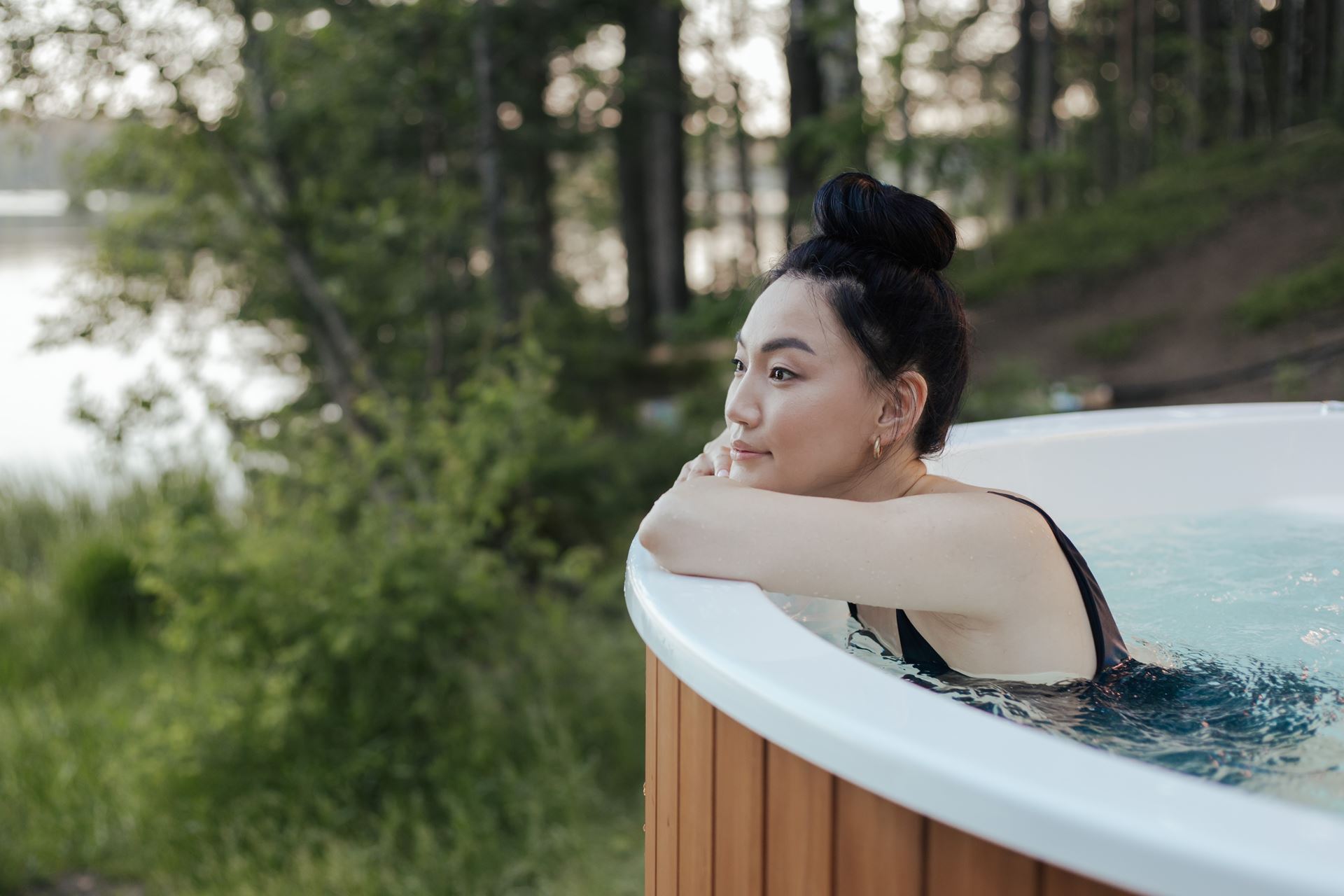 Woman soaks in hot tub looking out over forested area